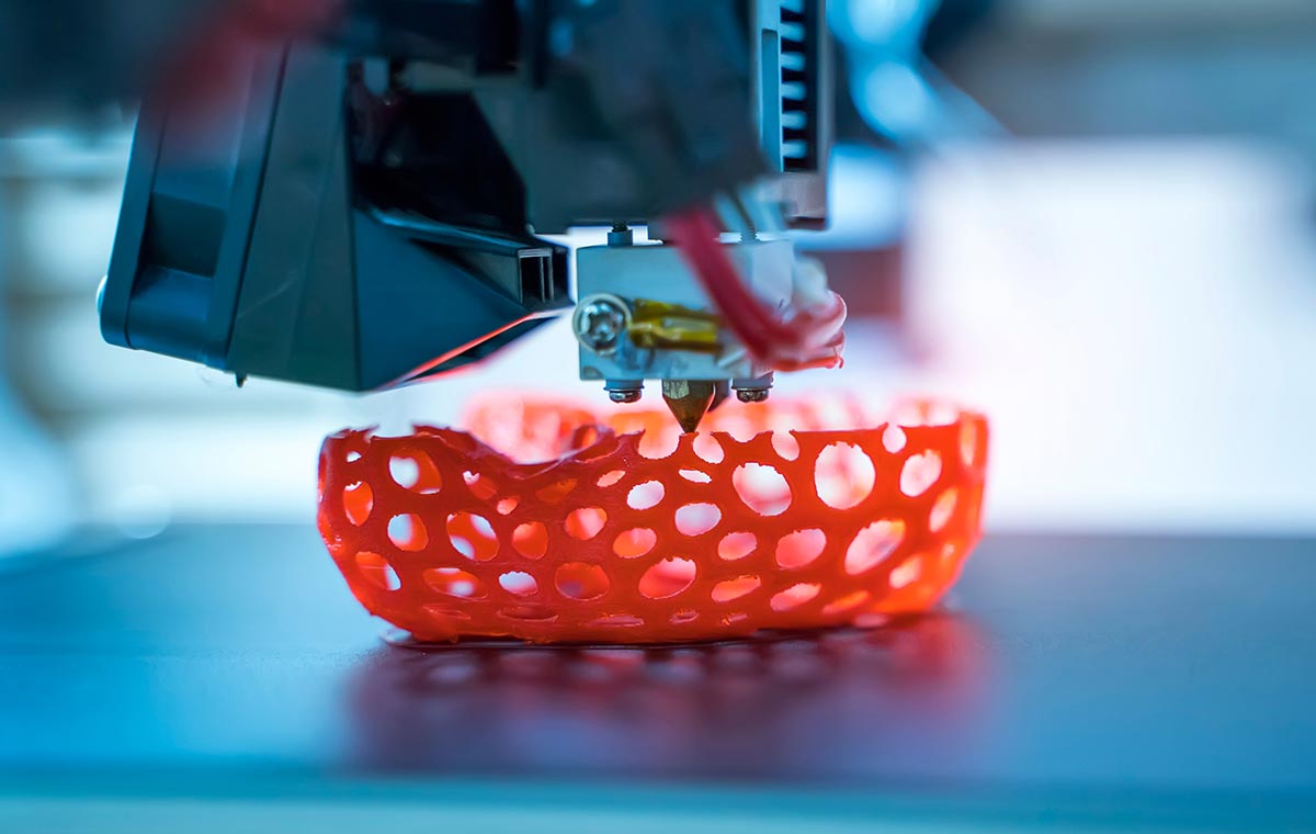A perforated orange bowl is 3D printed atop a metal surface